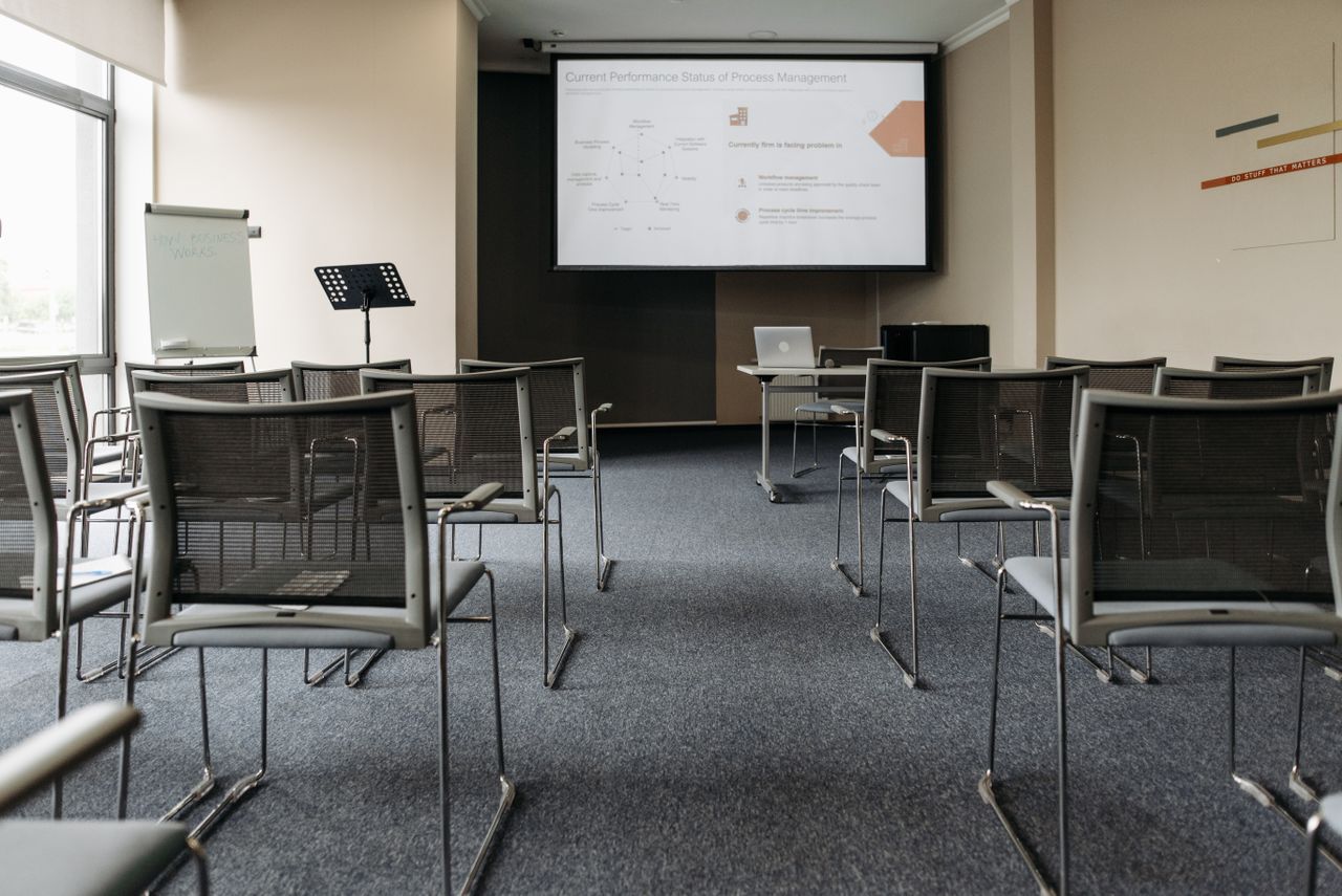 hero-img-01 An empty conference room with chairs, a projector screen, and presentation setup.